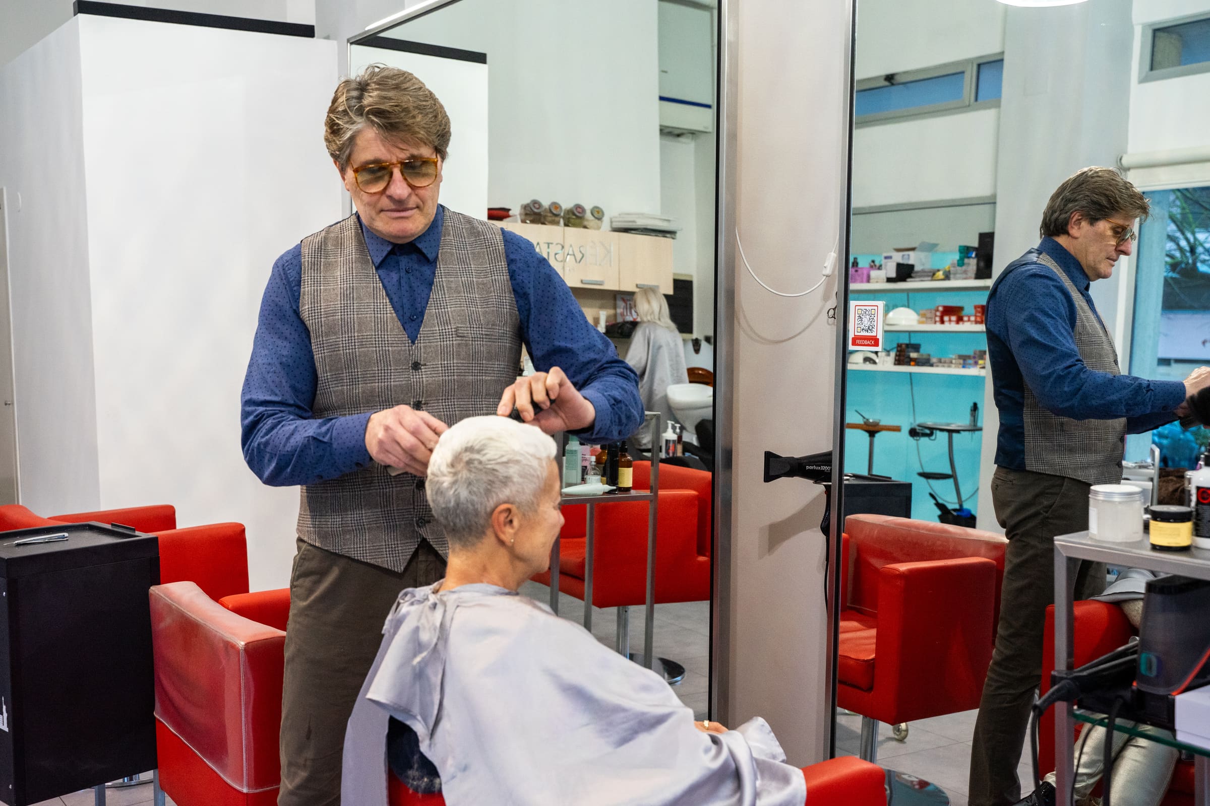 Marco Ballone al lavoro sui capelli di una cliente nel salone di Pescara, tra specchi e poltrone rosse